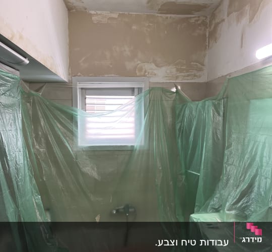 חדר אמבטיה עם קירות מתקלפים ויריעות פלסטיק